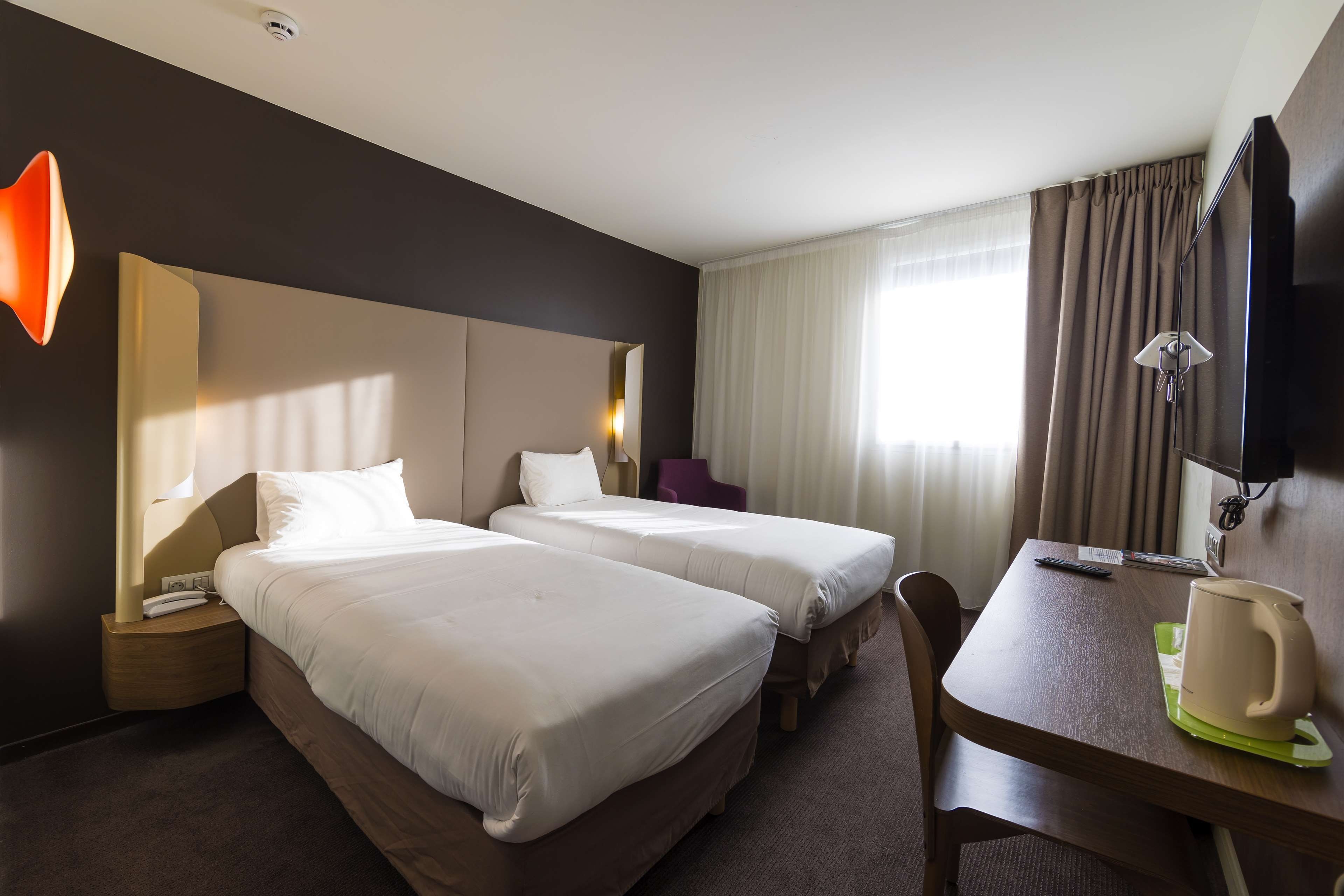 Een hotelkamer met twee bedden, een bureau, een stoel, een televisie en een raam met gordijnen.