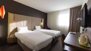 Een hotelkamer met twee bedden, een bureau, een stoel, een televisie en een raam met gordijnen.