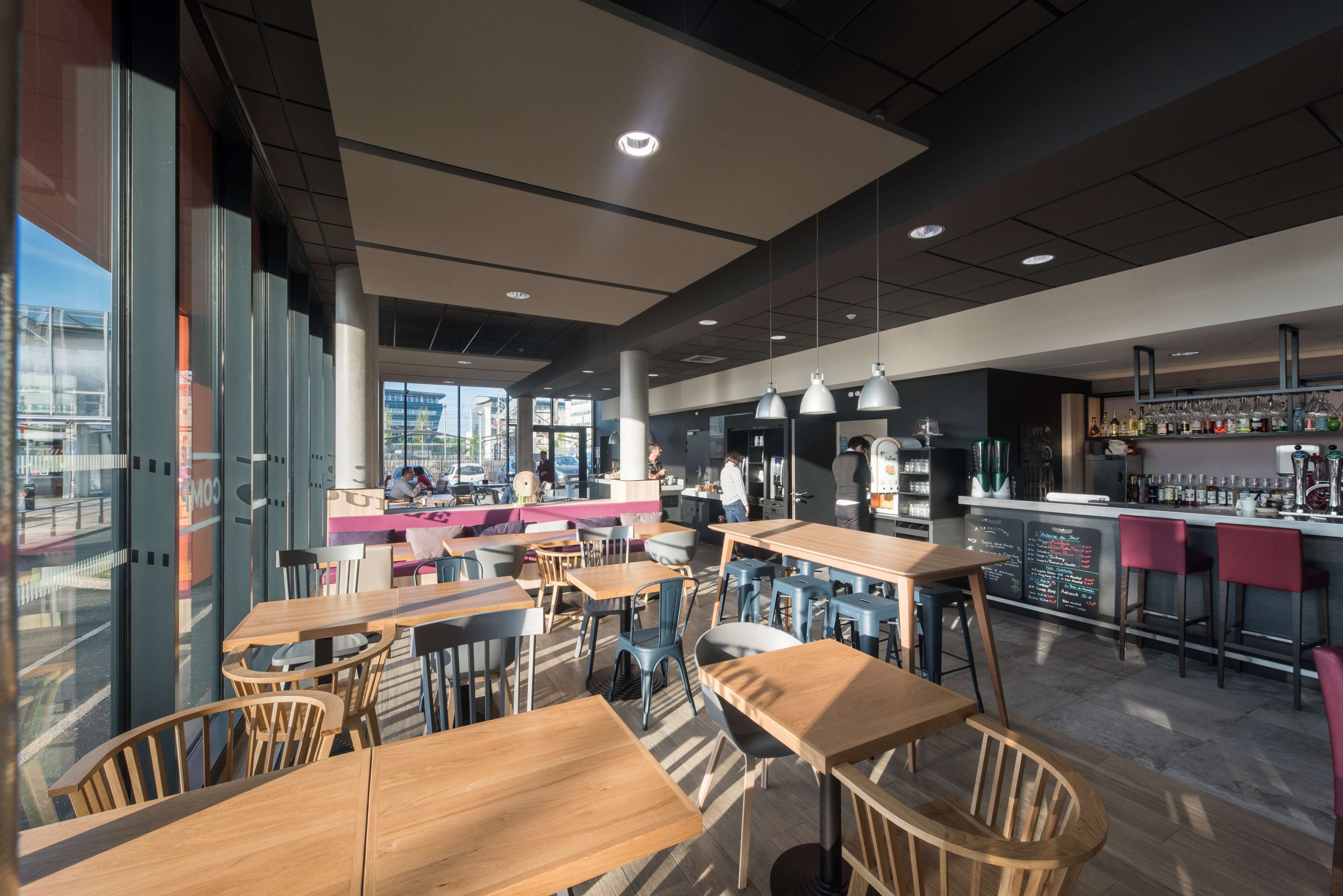 Un restaurante moderno con mesas y sillas de madera, una zona de bar con taburetes y vistas a la ciudad a través de amplios ventanales.