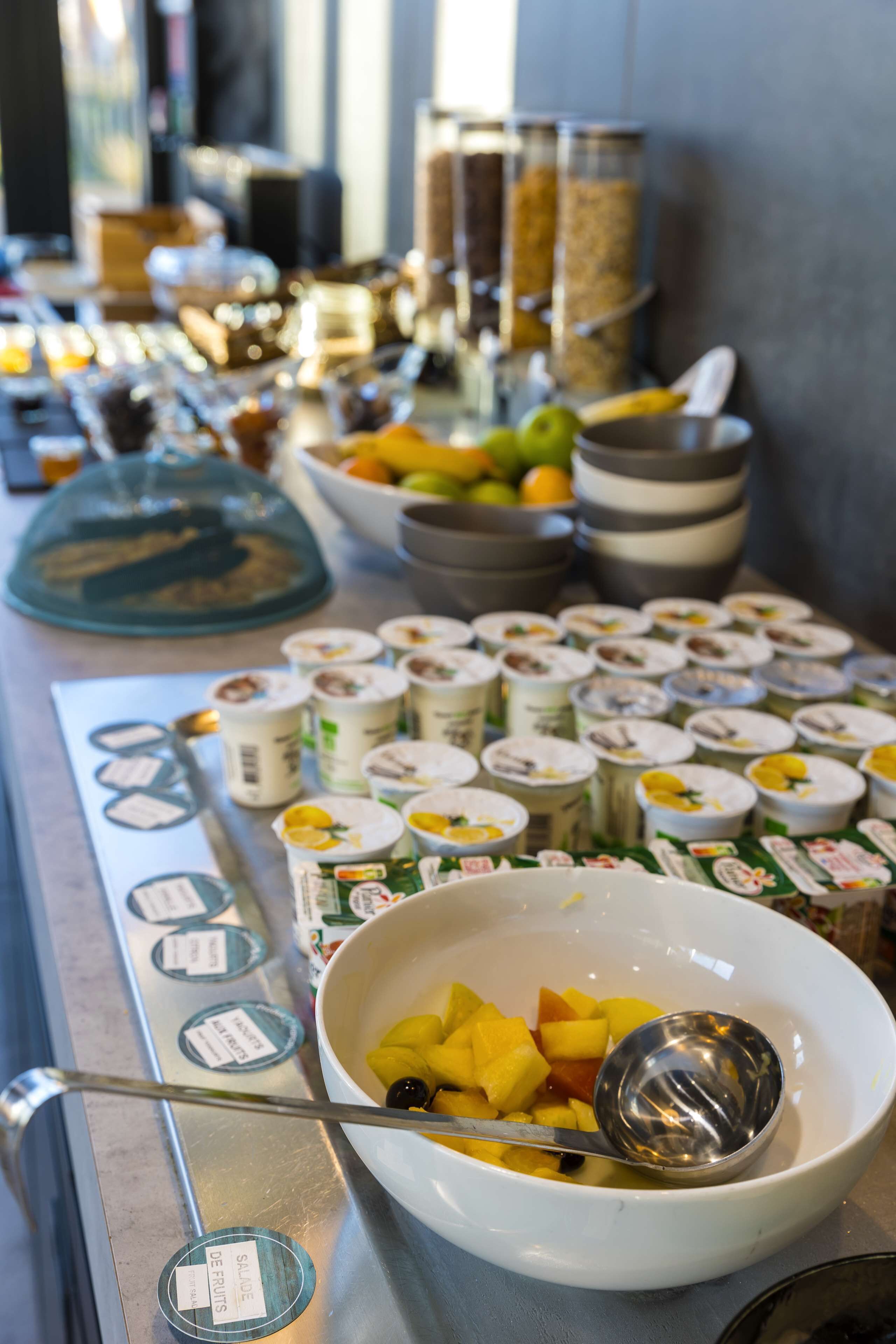A buffet with various food items and containers, including bowls of fruit and yogurt.