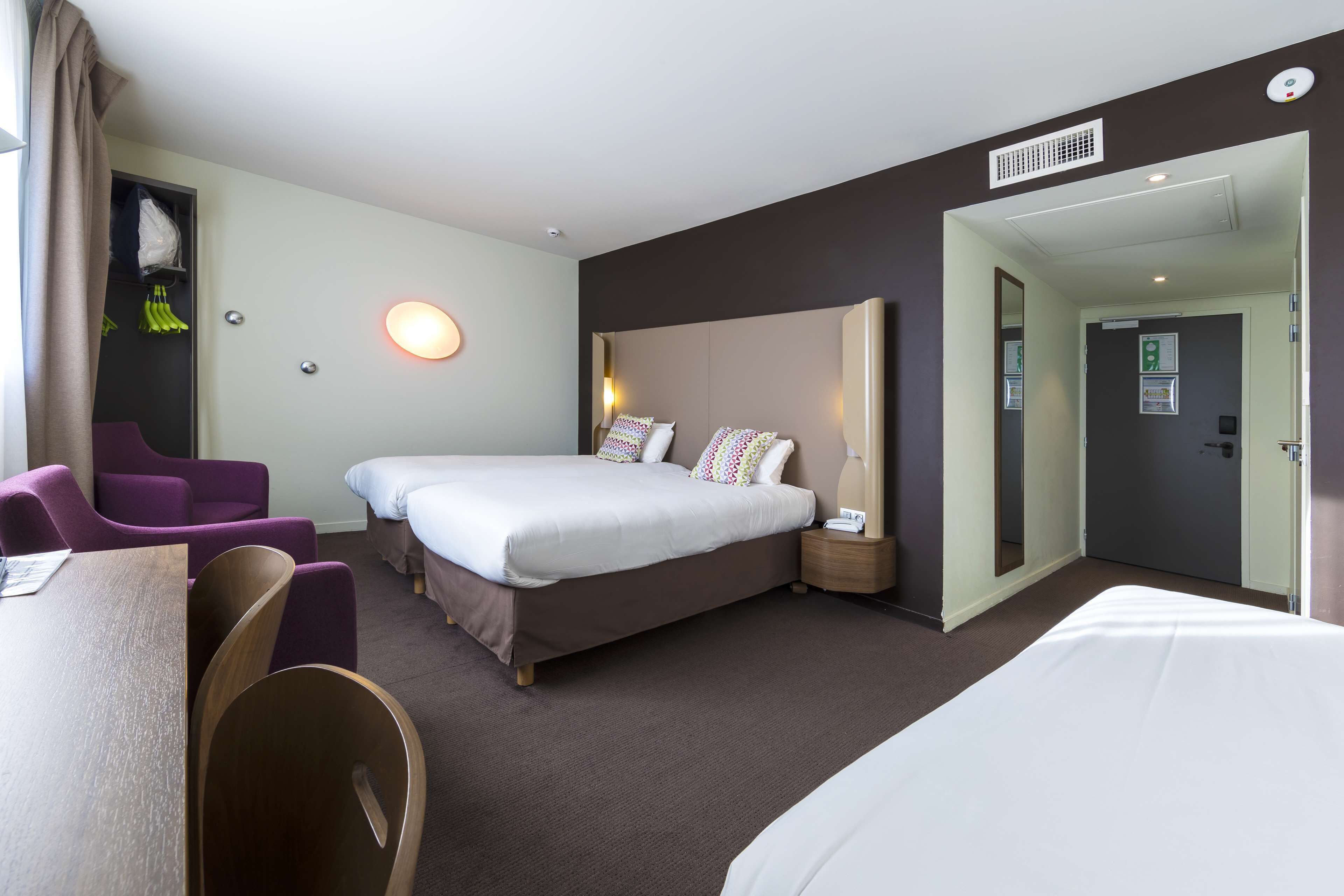 A hotel room with a large bed, two bedside tables, a desk, and purple chairs.