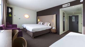 A hotel room with a large bed, two bedside tables, a desk, and purple chairs.