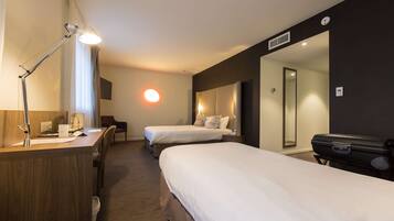 A hotel room with two beds, a desk with a lamp, a chair, and a suitcase.