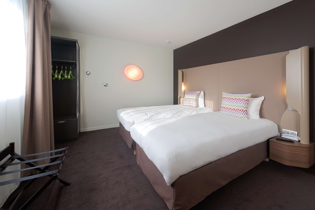 Ein Hotelzimmer mit einem großen Bett, einem Nachttisch mit Lampe, einem Kleiderschrank und einer Sitzbank.