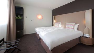 Une chambre d’hôtel avec un grand lit, une table de chevet avec une lampe, une armoire et un banc.