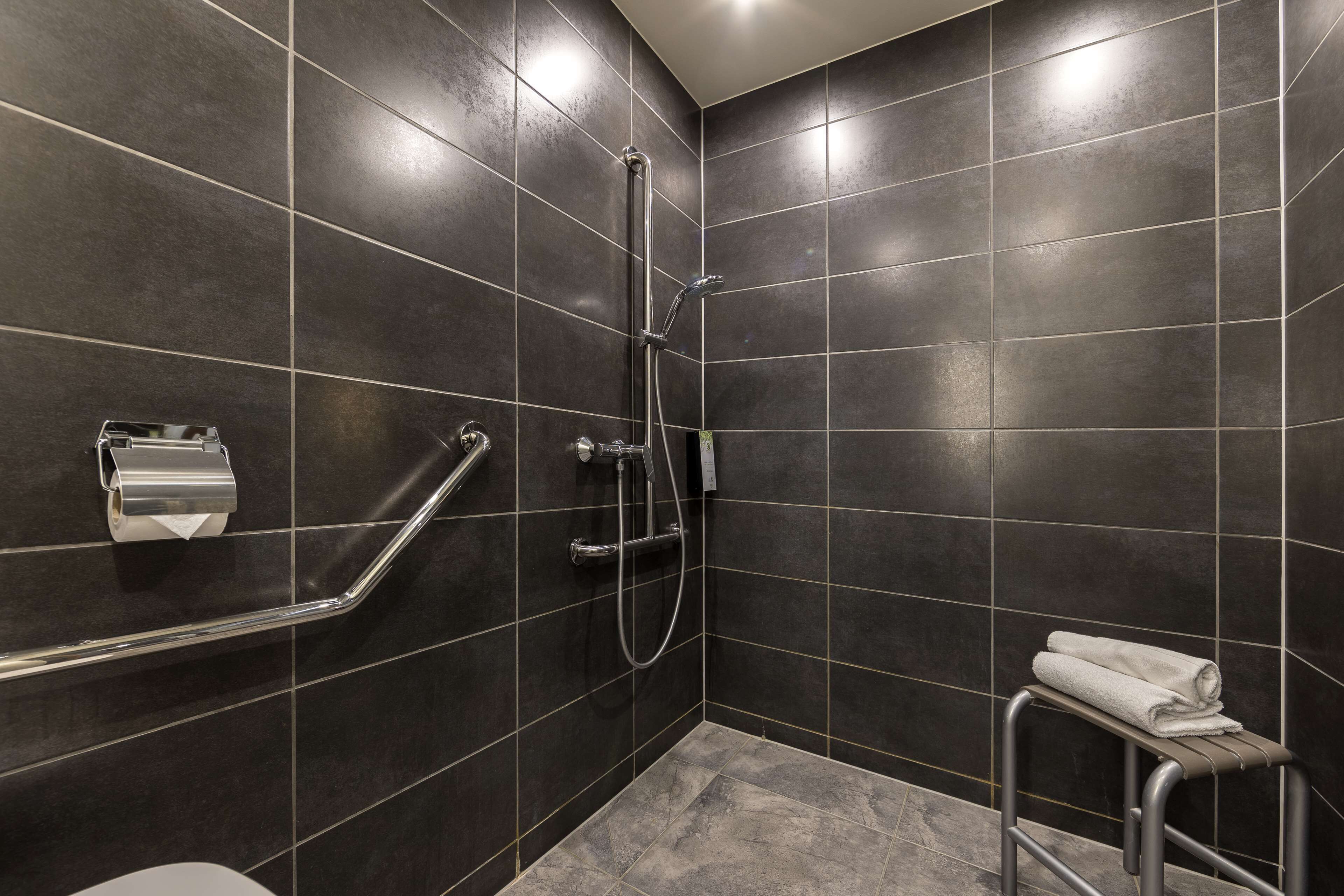 A modern bathroom with dark tiles, a shower, a toilet, and a towel rack.