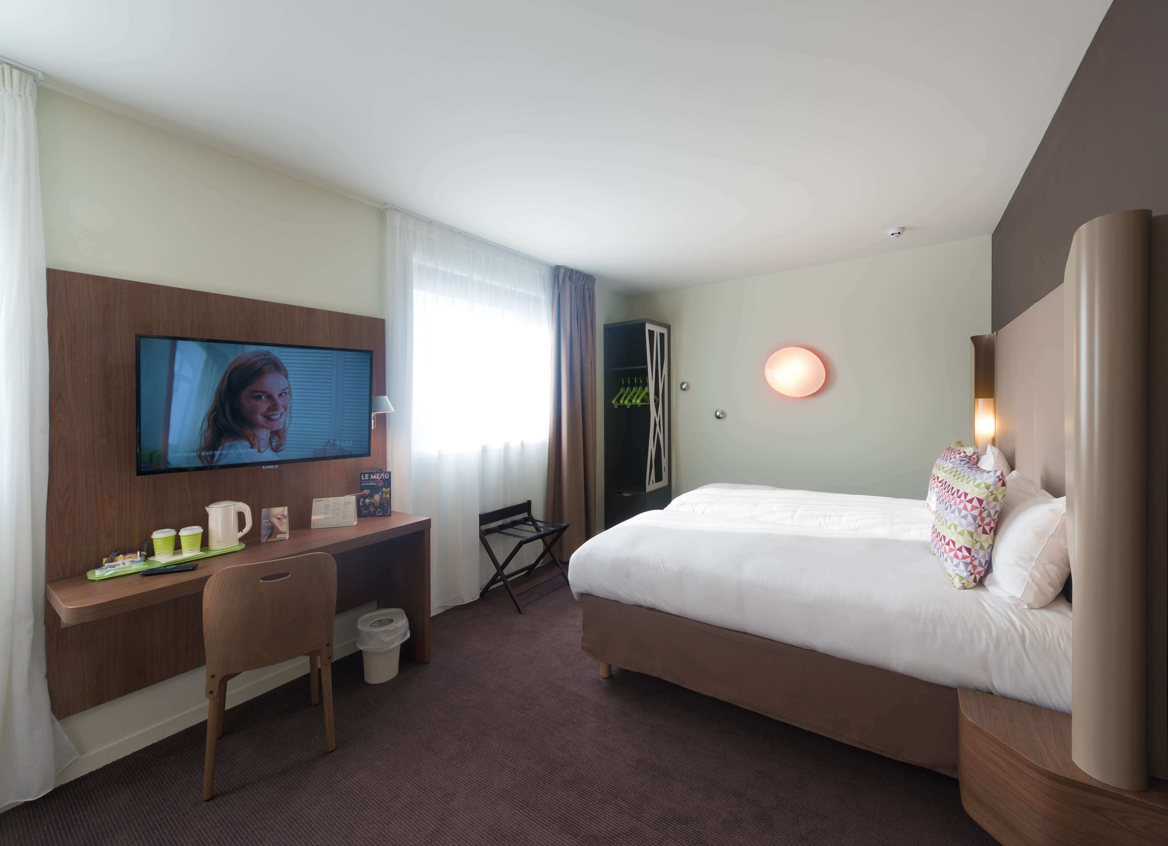 Une chambre d’hôtel comprenant un lit, un bureau avec une chaise, une télévision et une armoire.