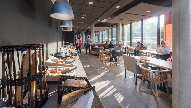 Un restaurant moderne avec de longues tables conviviales, des paniers à pain en osier et des luminaires suspendus.