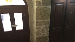 Una habitación con pared de piedra, una puerta de madera con ventana y suelo de baldosas.