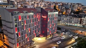 A modern building with a prominent 'RAMADA' sign, multiple floors, and a street view with vehicles and a bridge in the background.