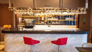 Una cocina moderna con encimera de mármol, dos taburetes rojos y una zona de bar con copas de vino colgando.