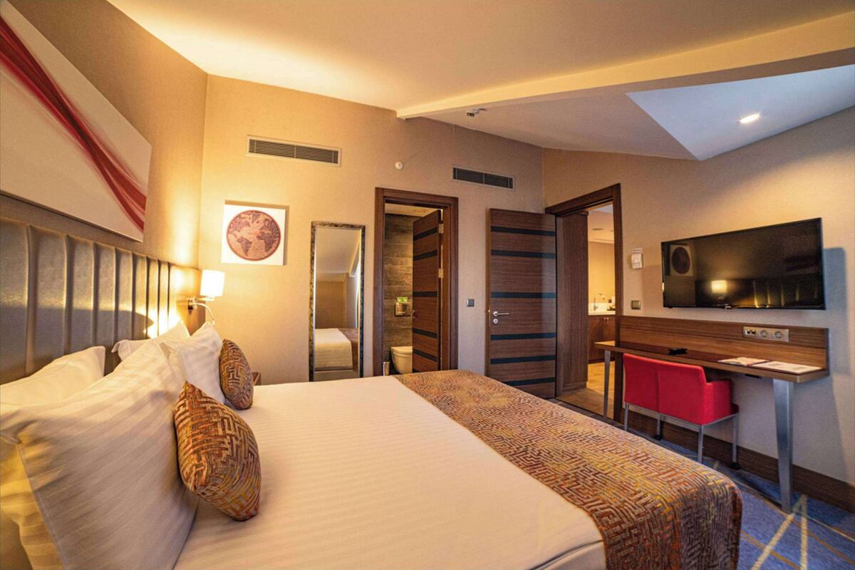 A hotel room with a large bed, a desk, a TV, and a bathroom visible through an open door.