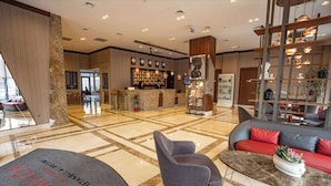 A hotel lobby with a reception desk, seating area, and a decorative wall with shelves.