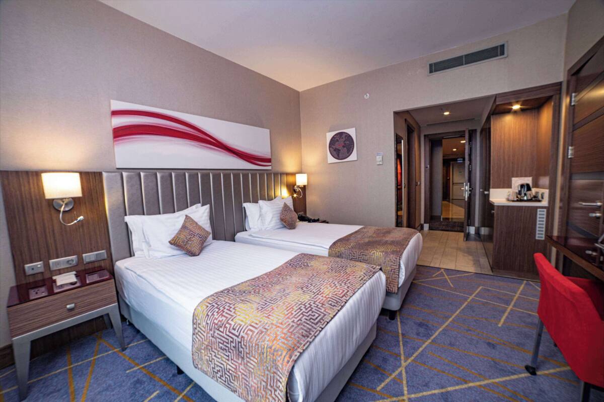 A hotel room with two beds, a desk, a chair, a bathroom, and a large abstract painting on the wall.