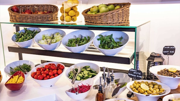 A buffet with various food items including salads, fruits, and olives.