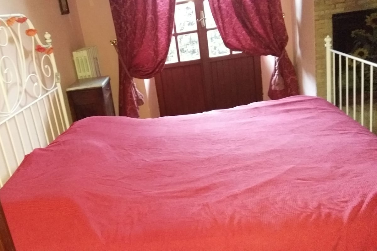 Quarto com cama, cómoda de madeira, janela com cortinas e radiador.