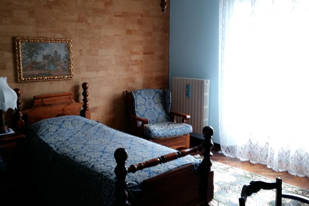 Quarto com cama de madeira, uma cadeira, abajur e um quadro na parede.