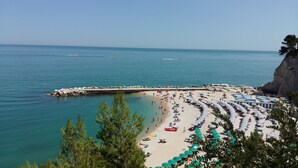 A beach with a rocky coastline, clear blue water, and numerous umbrellas and sun loungers. - Villa Anna (Osimo)