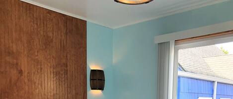 Un dormitorio con una cama grande, pared de paneles de madera y ventana con vistas a un edificio azul.