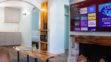 Una sala de estar con televisión de pantalla plana mostrando servicios de transmisión, chimenea y área de cocina con armarios.