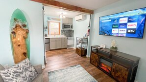 A modern living room with a flat-screen TV displaying streaming services, a fireplace, and a kitchen in the background.