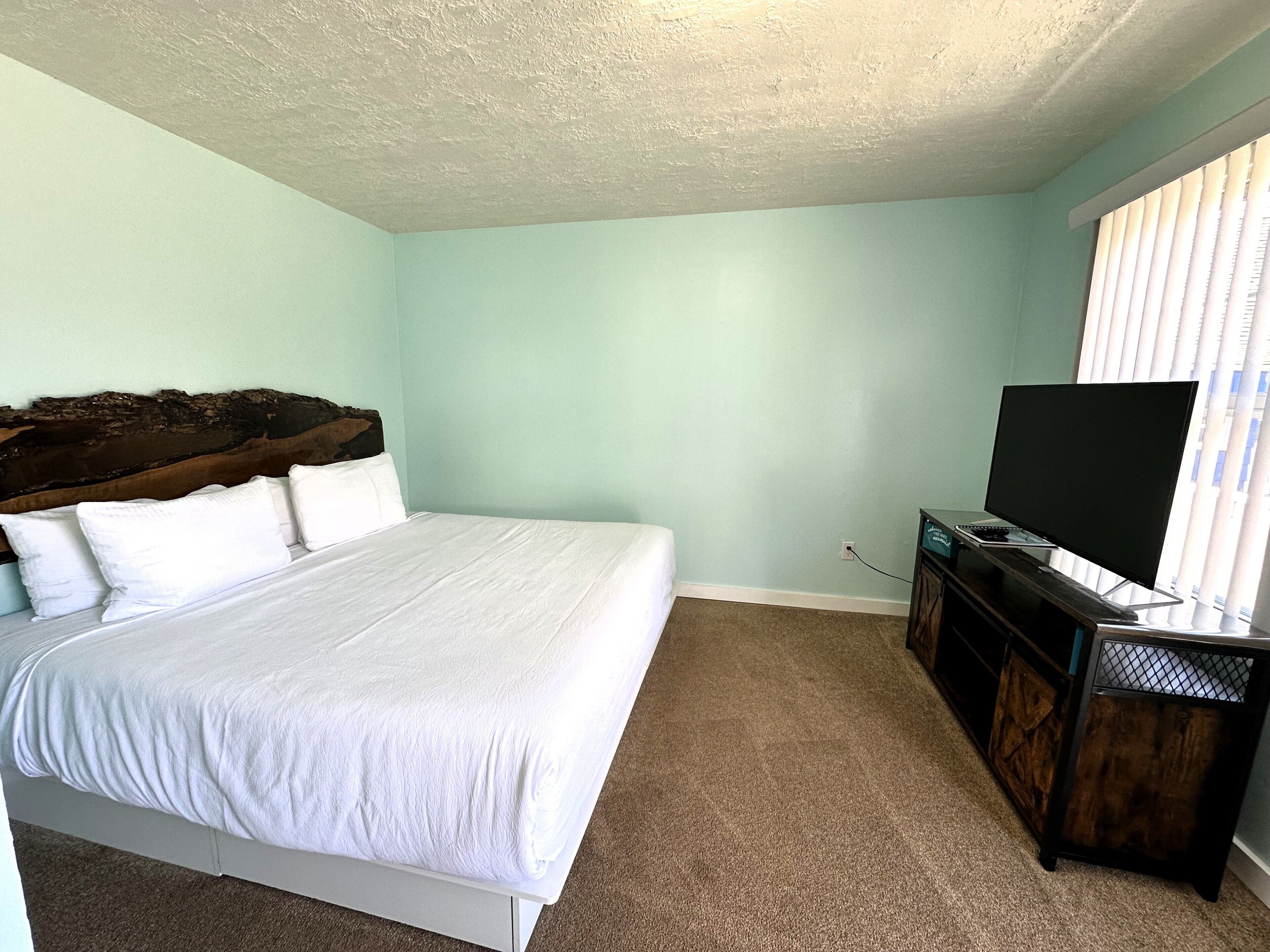 Un dormitorio con una cama, un televisor sobre un mueble y una ventana con persianas.