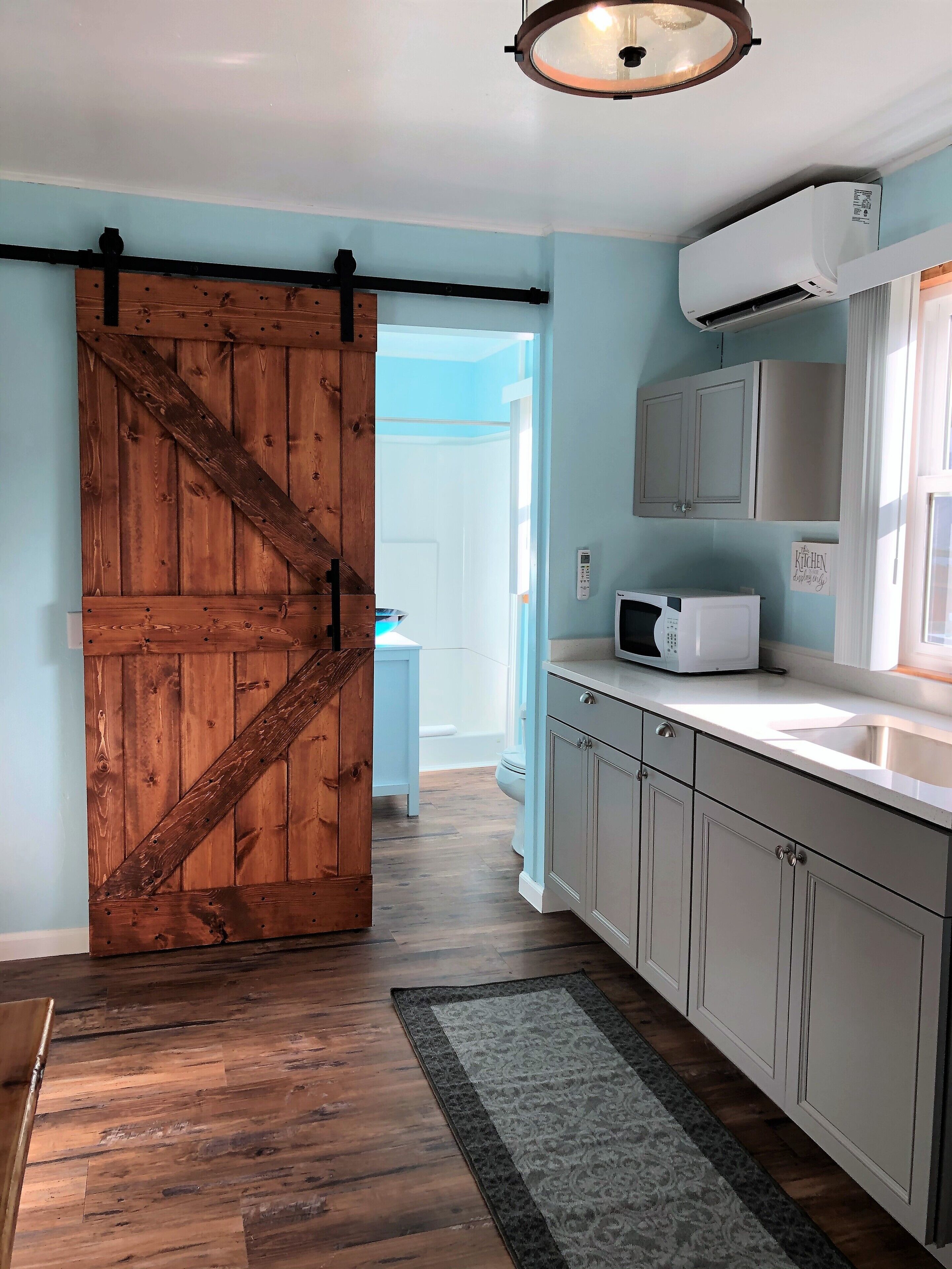 A kitchen with a wooden barn door, a microwave, cabinets, and a rug.
