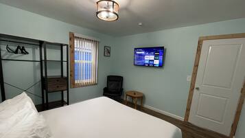 A bedroom with a bed, a TV mounted on the wall, a wooden door, and a window with blinds.