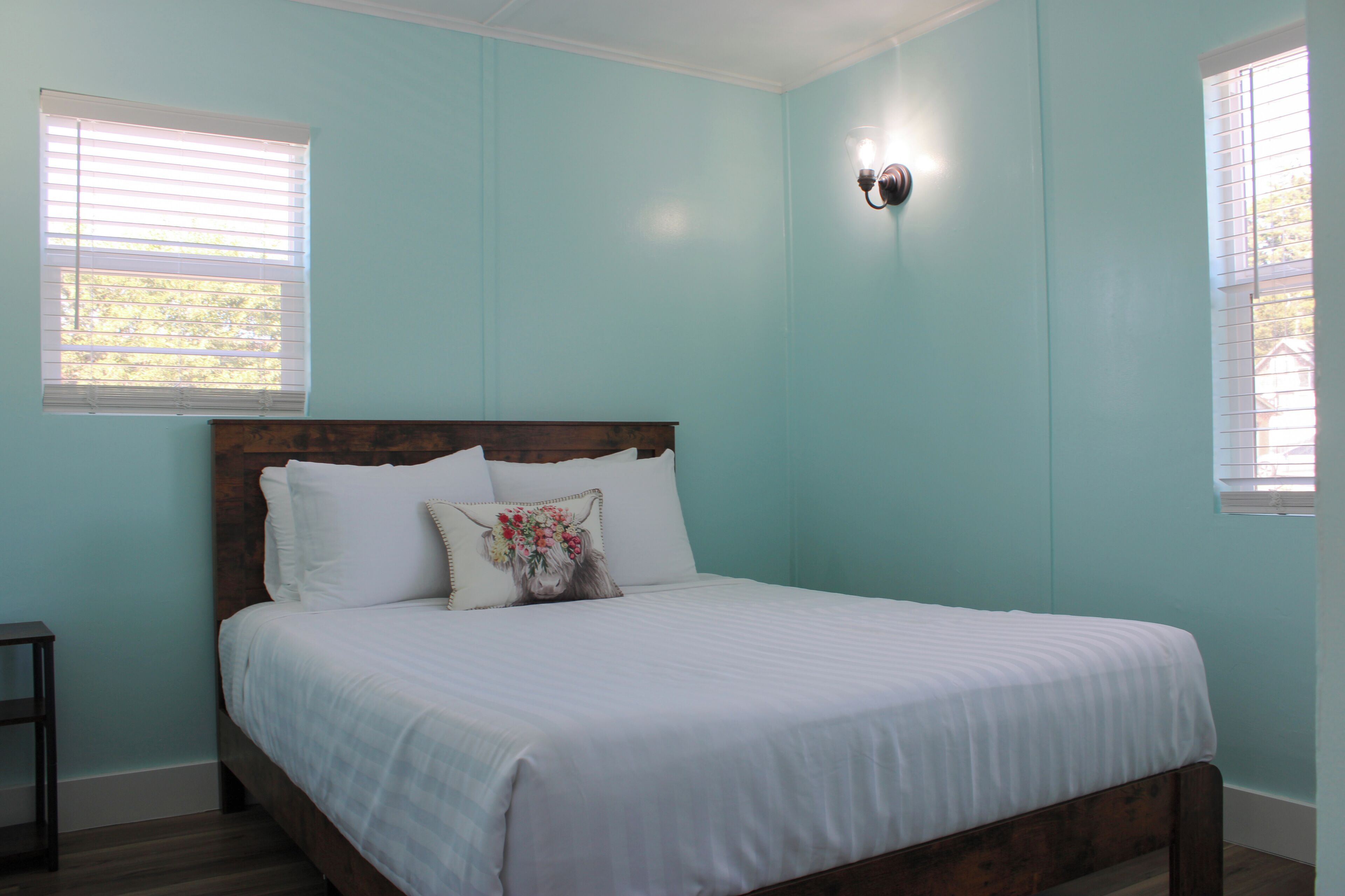 A bedroom with a bed, white bedding, a wooden headboard, and a wall-mounted light fixture.
