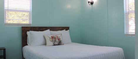 A bedroom with a bed, white bedding, a wooden headboard, and a wall-mounted light fixture.