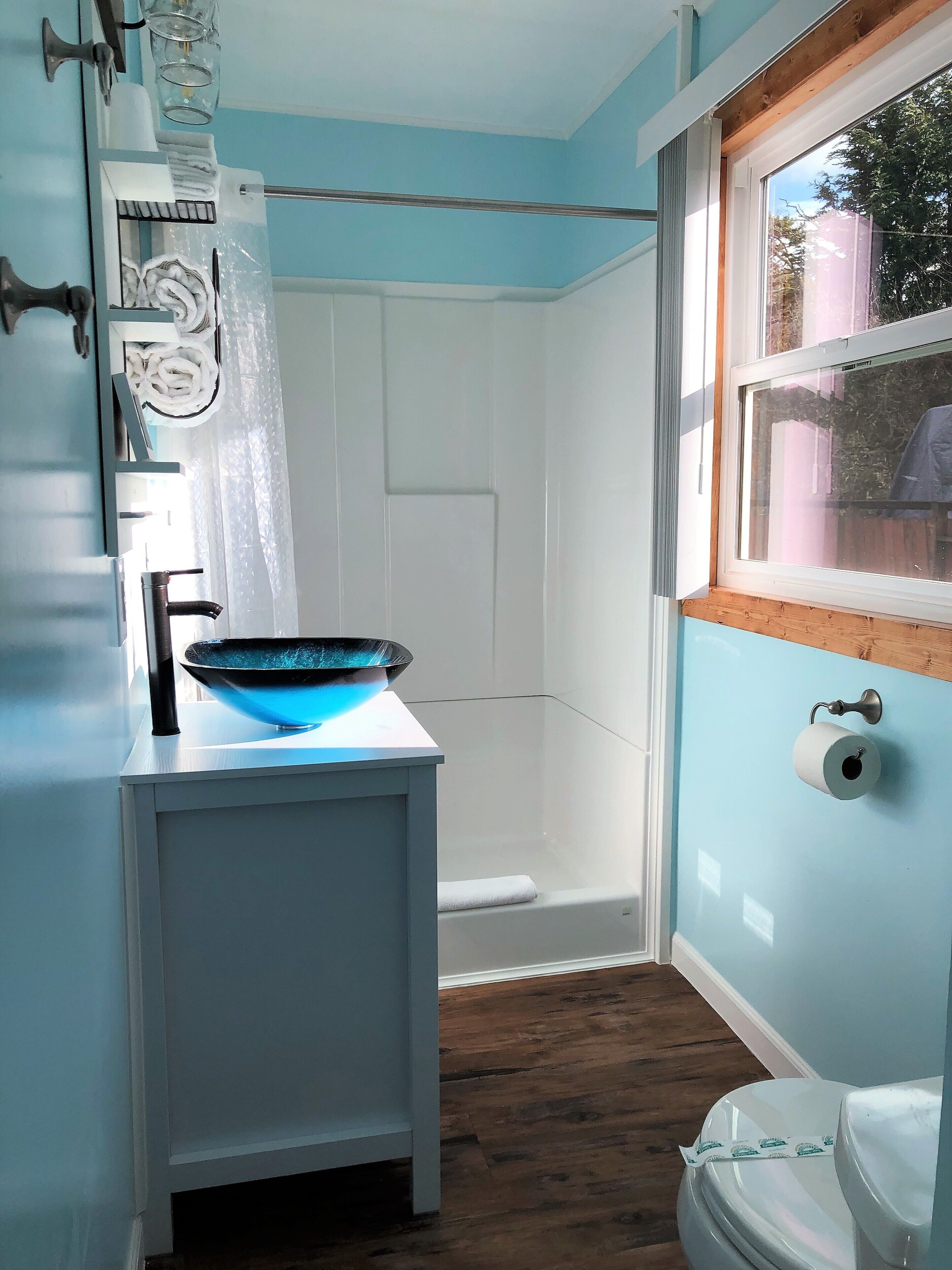 A bathroom with a blue wall, a white toilet, a blue basin, and a shower area.