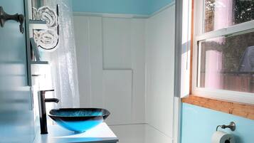 A bathroom with a blue wall, a white toilet, a blue basin, and a shower area.