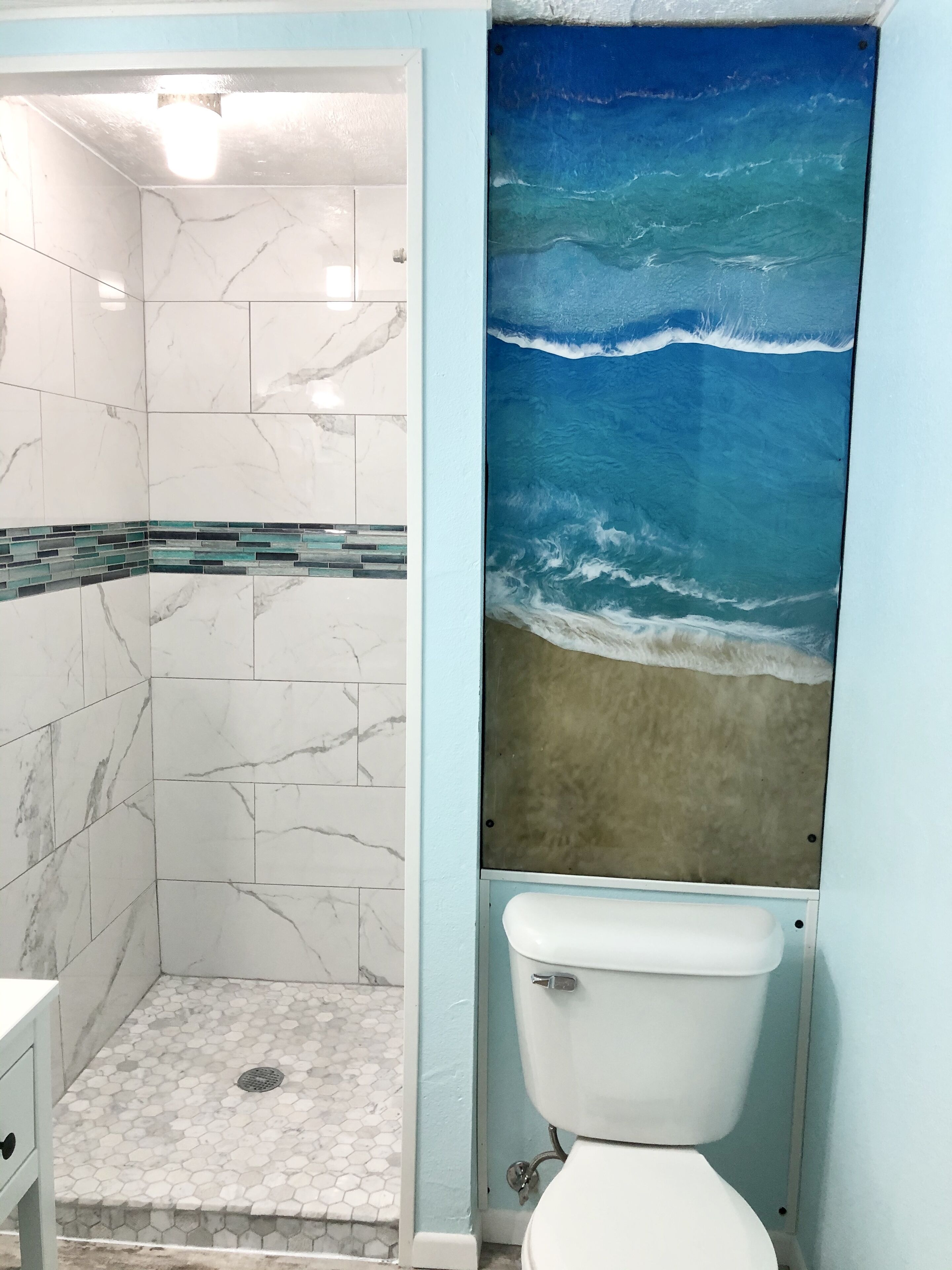 Une salle de bain avec une douche, des toilettes et un mur orné d’une fresque représentant un paysage marin.