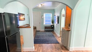A hallway with a black refrigerator, a wooden counter, a blue rug, and a door leading to another room.