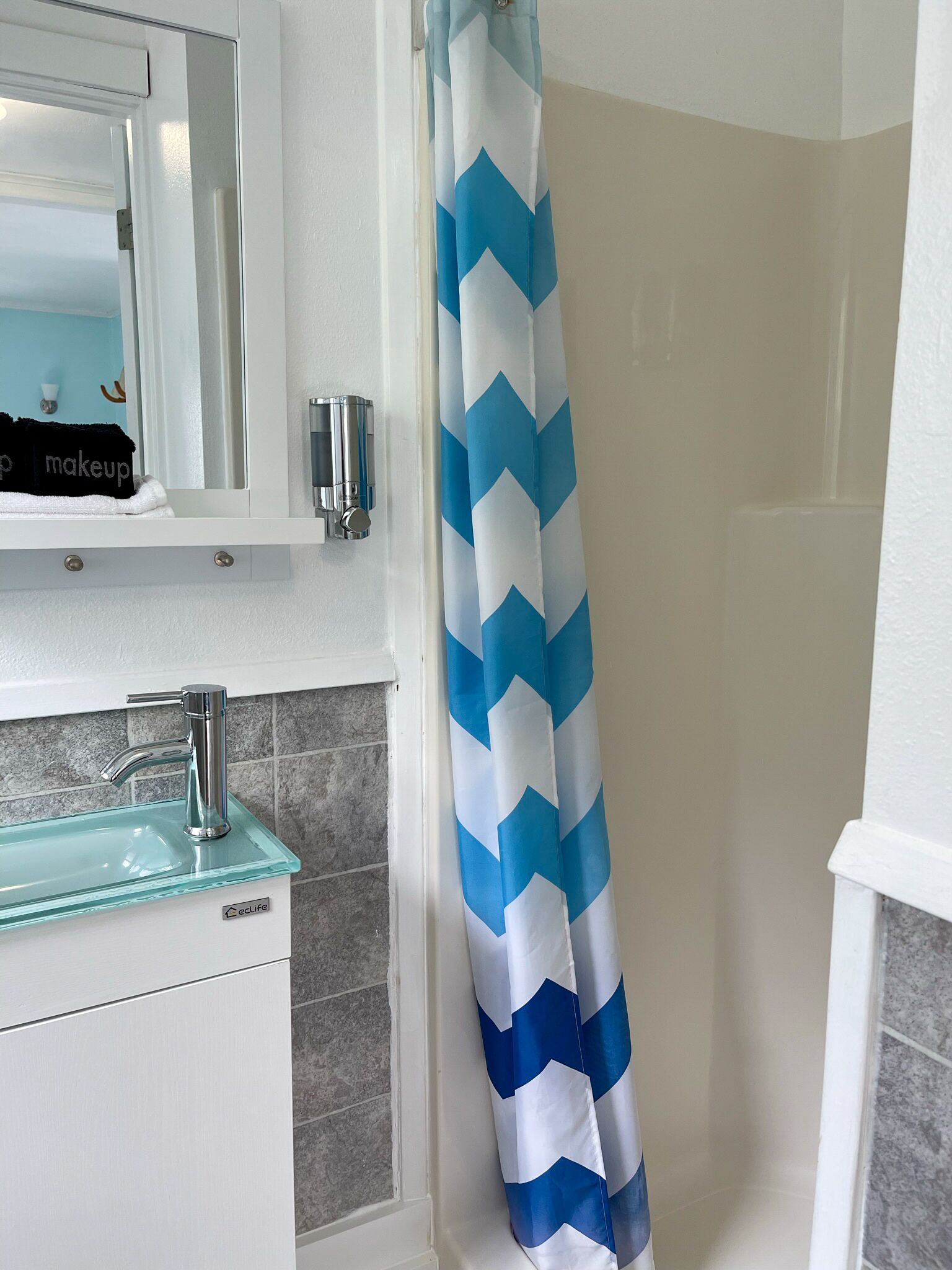 Een badkamer met een witte wastafel, een spiegel en een douchegordijn met een blauw-wit ruitpatroon.