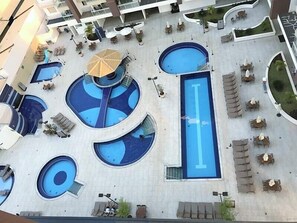 Uma área de piscina no terraço, com várias piscinas, espreguiçadeiras e guarda-sóis.