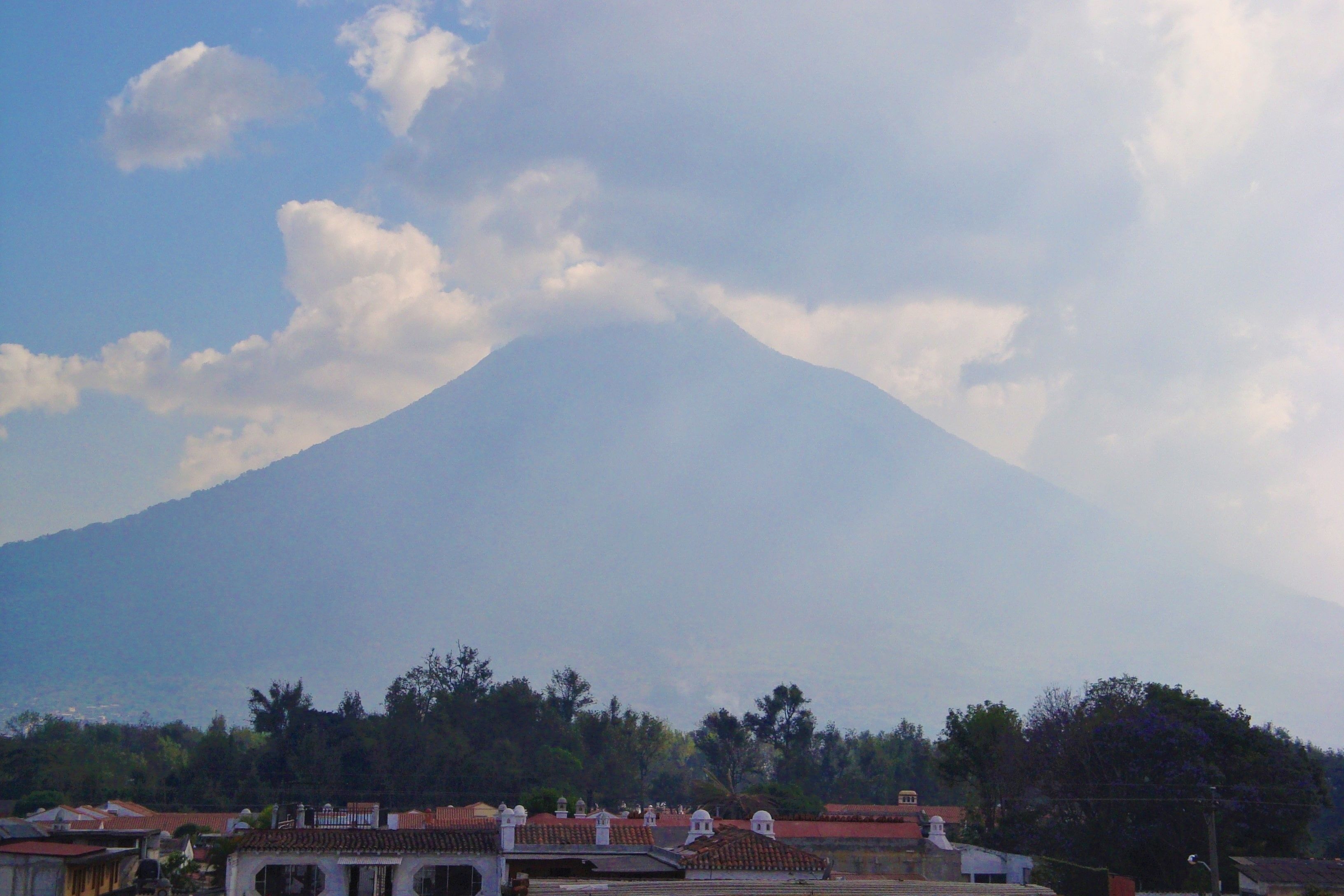 Una montaña con un edificio al frente, con techo de tejas rojas.