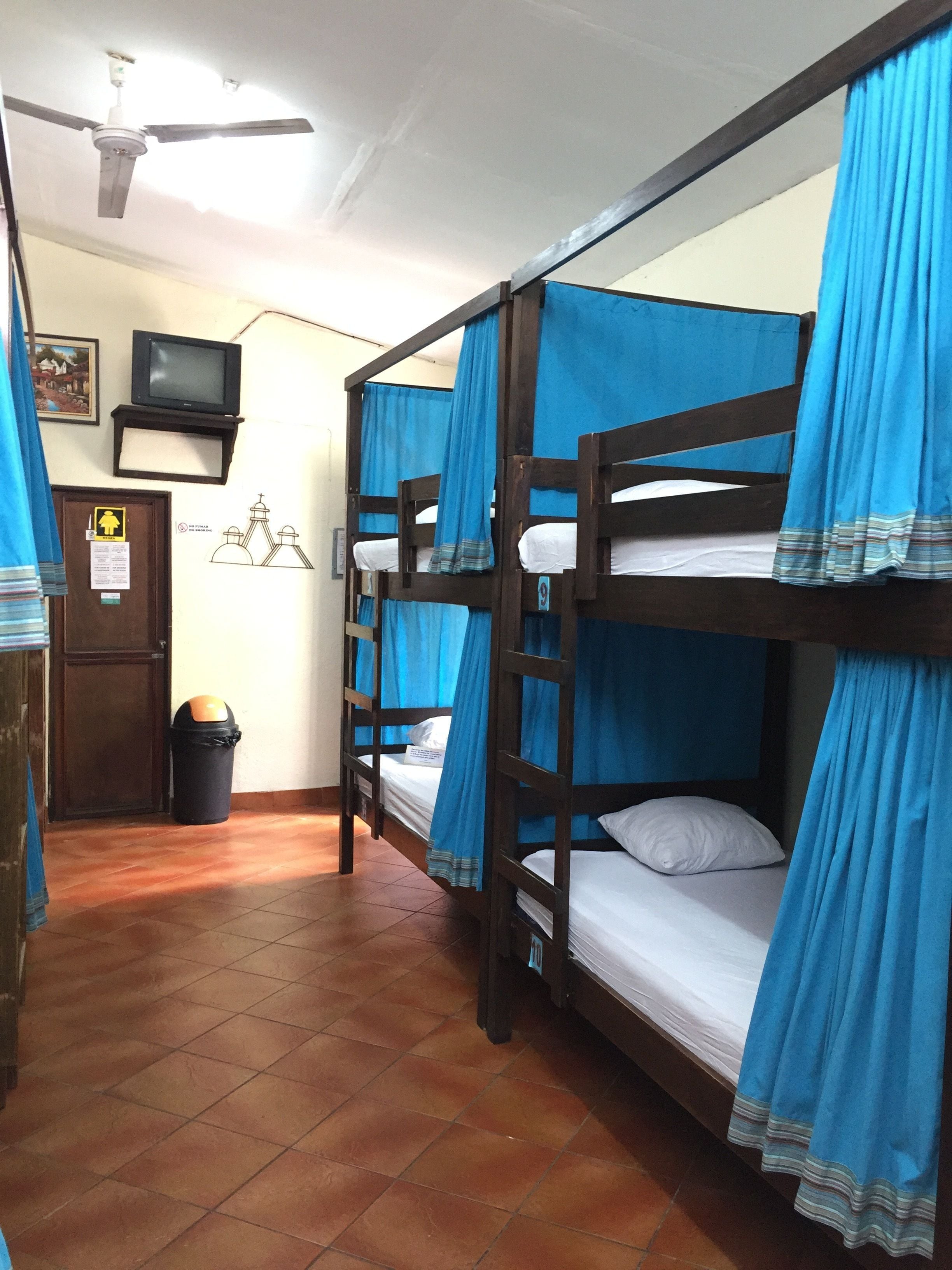 Una habitación con literas, ventilador de techo, televisor y un cubo de basura.