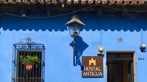 Un edificio azul con un letrero que dice 'Hostal Antigua' y un perro sentado afuera.