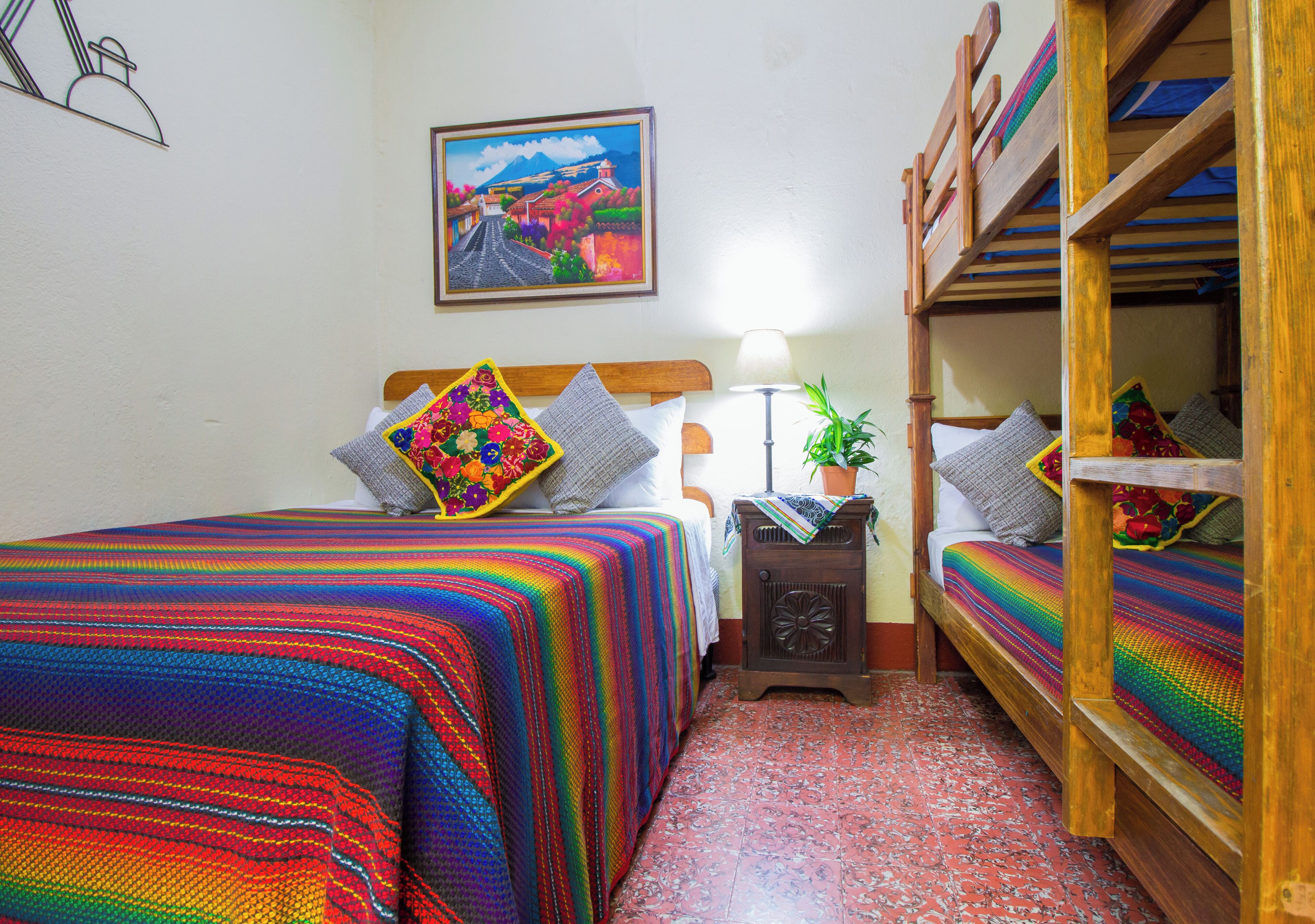 A room with a bed, a nightstand, a lamp, a potted plant, and a painting on the wall.