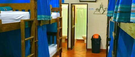 A dormitory room with bunk beds, a ceiling fan, a television, and a tiled floor.