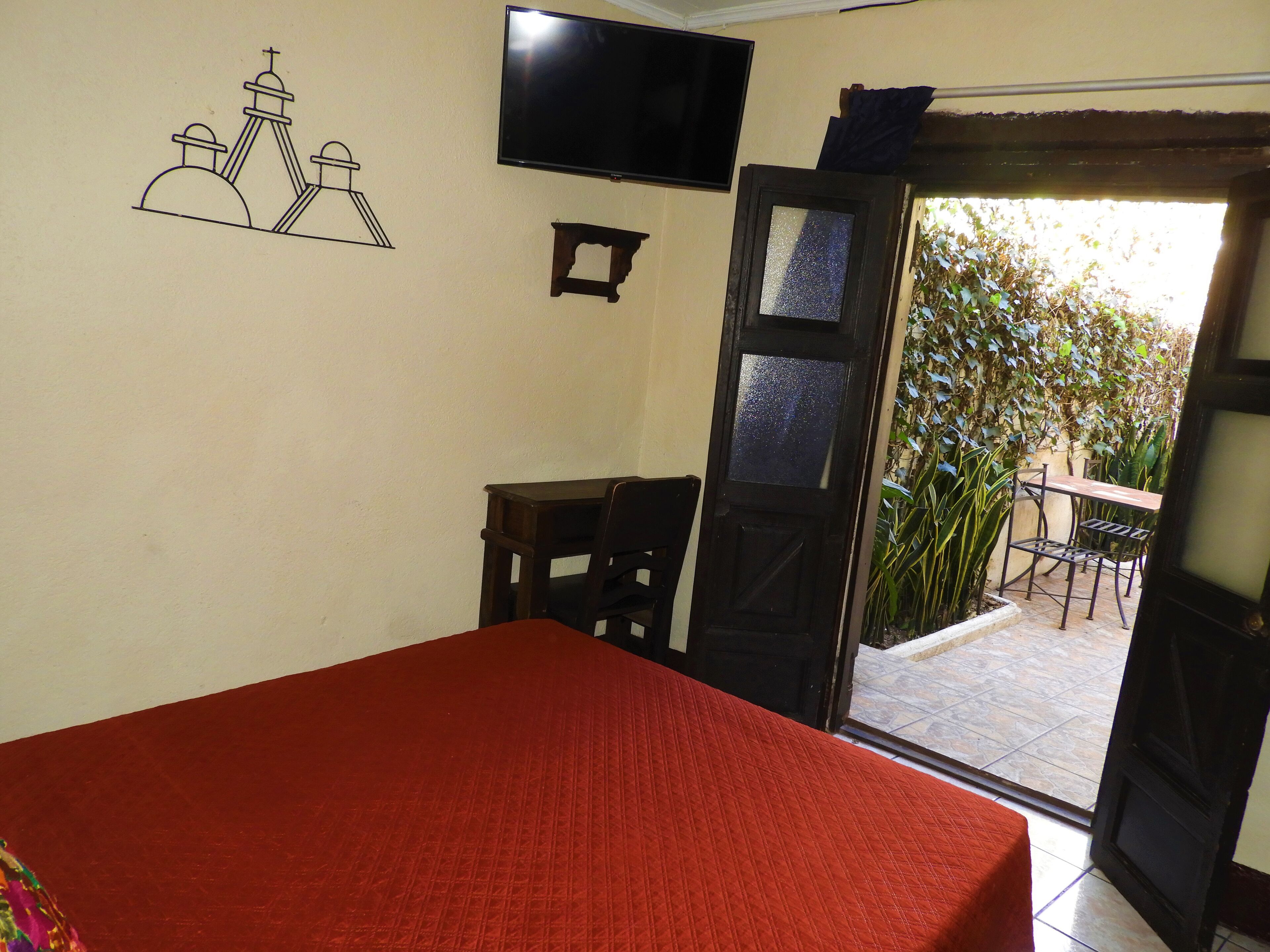 A room with a bed, a TV mounted on the wall, and a door leading to an outdoor patio area with a table and chairs.