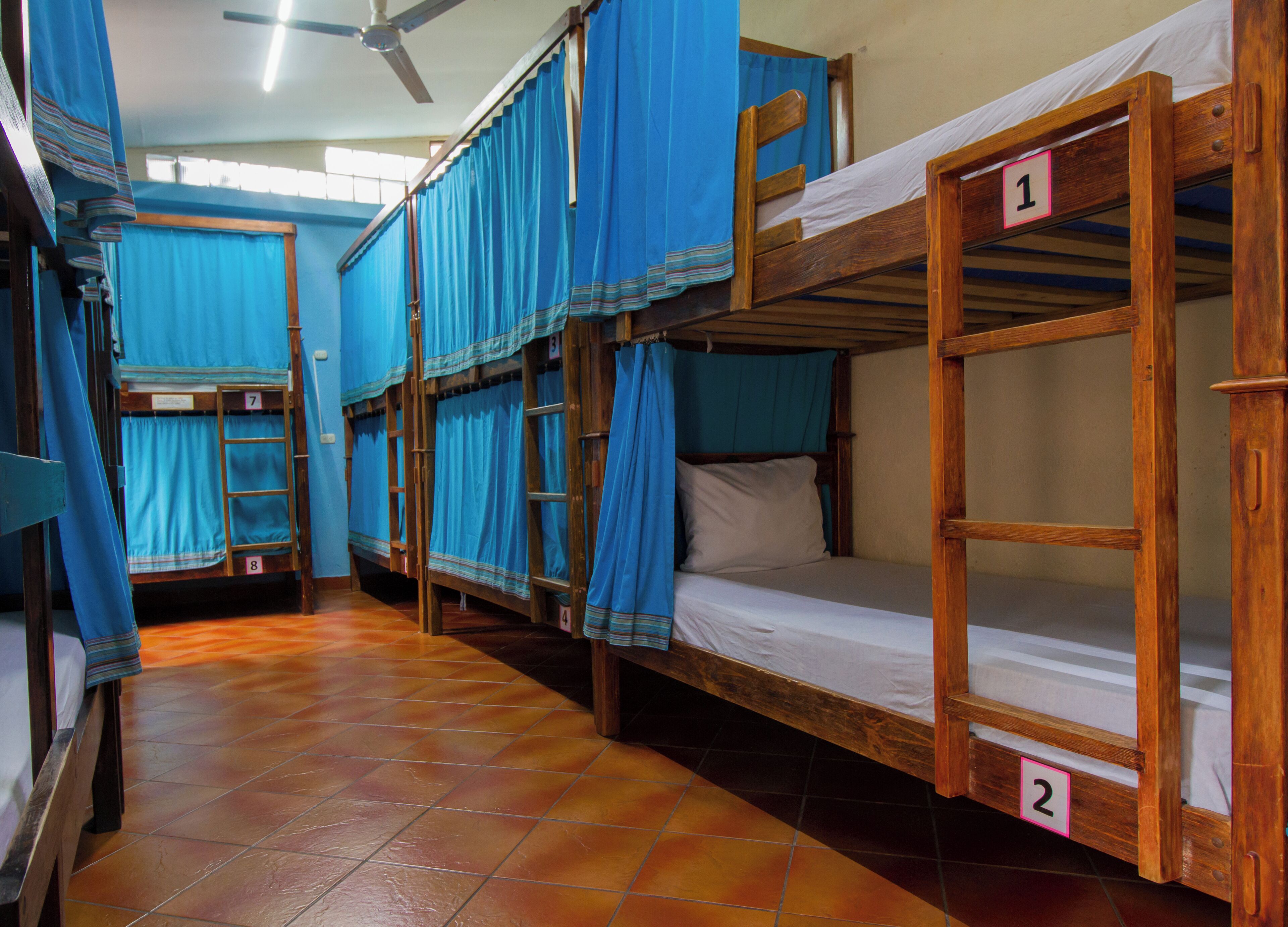 A dormitory room with bunk beds, numbered beds, and blue curtains.