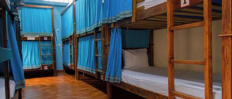 Une chambre de dortoir avec des lits superposés, des lits numérotés et des rideaux bleus.