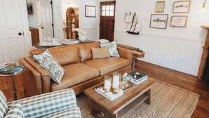 A living room with a brown leather sofa, a wooden coffee table, and framed fish pictures on the wall. - The Cottages at Bigfork (Bigfork)