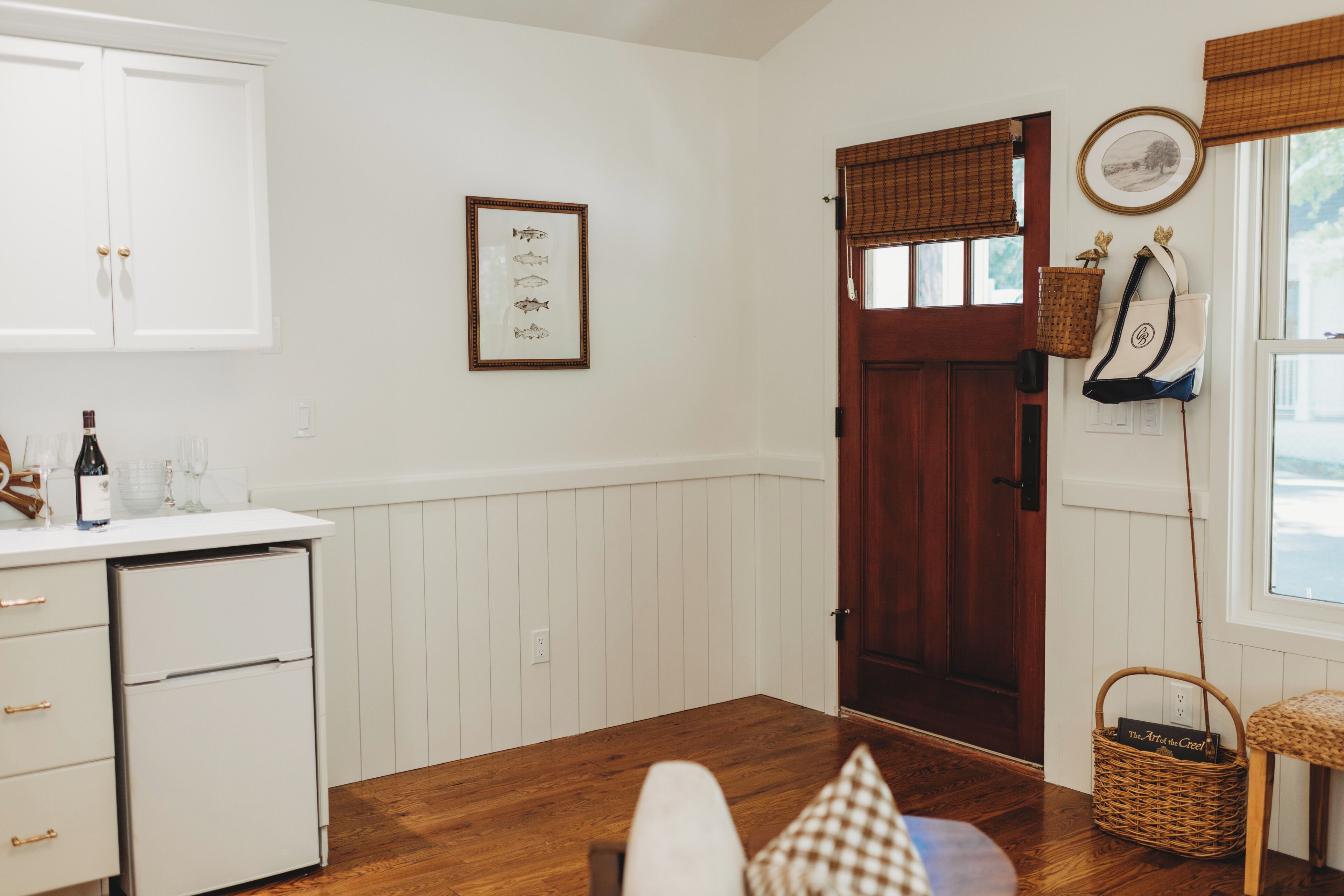 A kitchen with white cabinets, a wooden door, a wicker basket, and a framed picture on the wall.