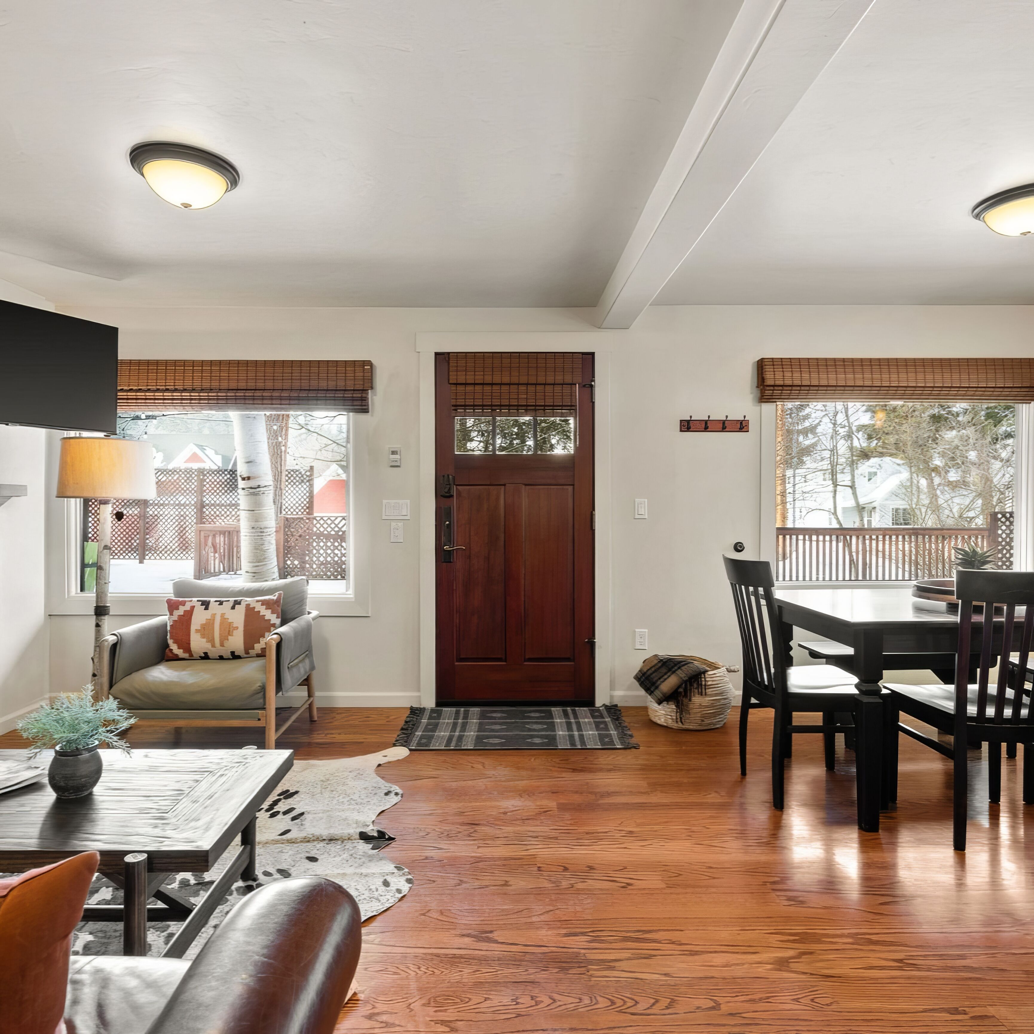 A spacious living area with a wooden dining table, a sofa, and a TV mounted on the wall.