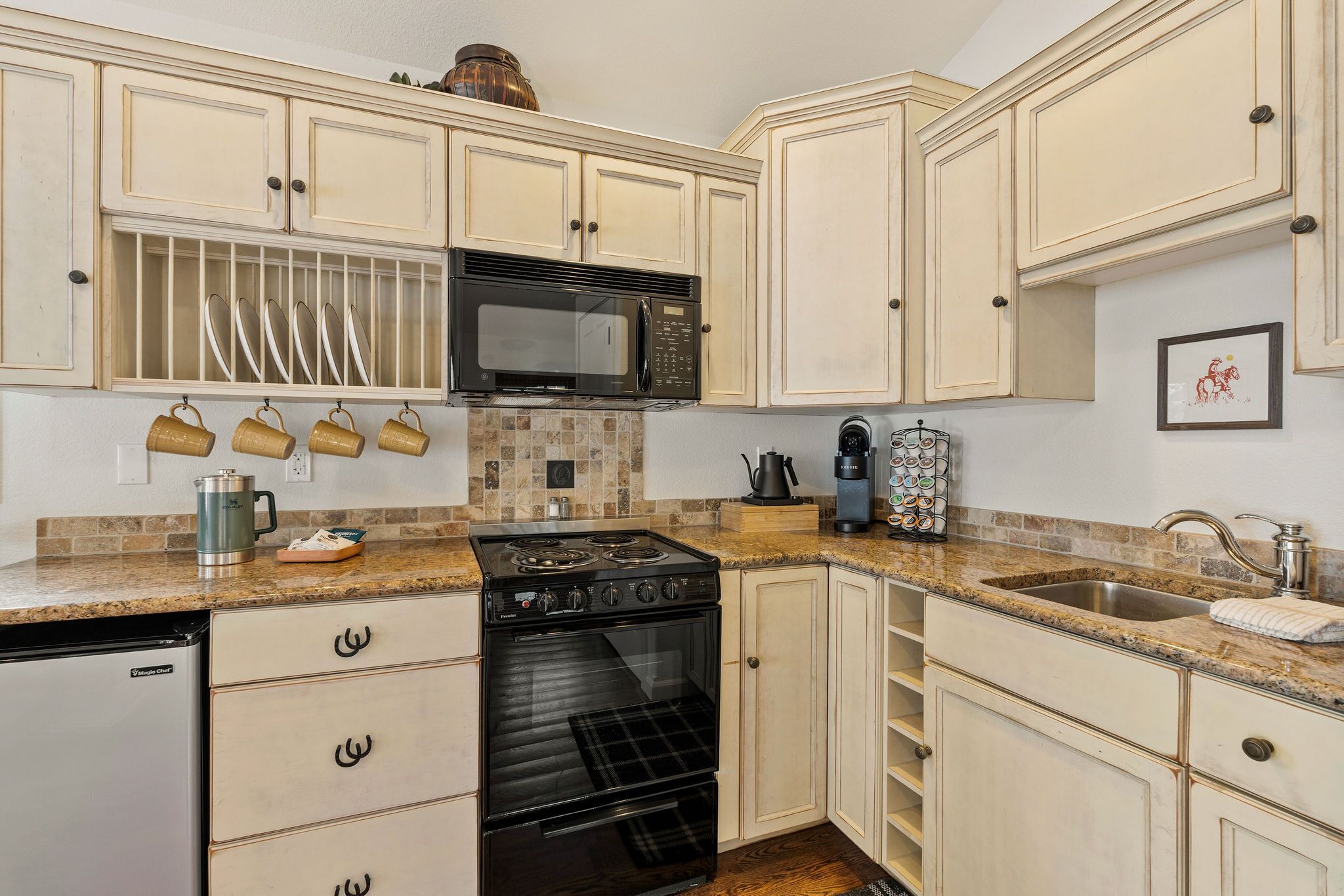 A kitchen with white cabinets, a black stove, a microwave, and a sink.