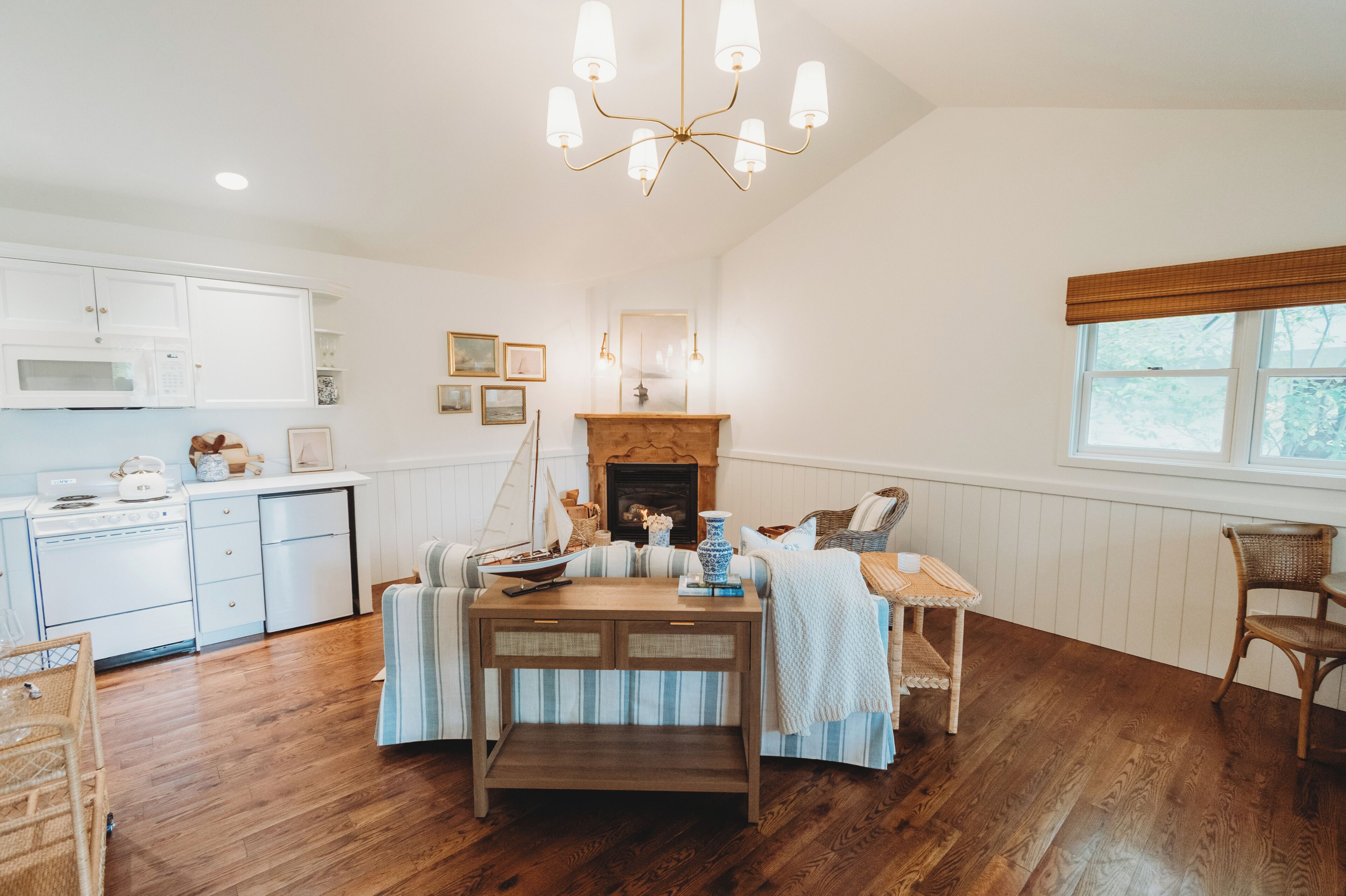 A kitchen with white cabinets, a microwave, and a stove. There is a dining area with a table, chairs, and a fireplace.