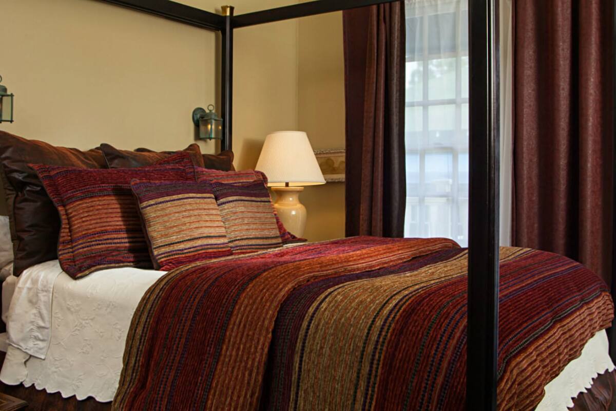 A neatly made bed with a striped blanket, two bedside lamps, and a mirror above the bed.